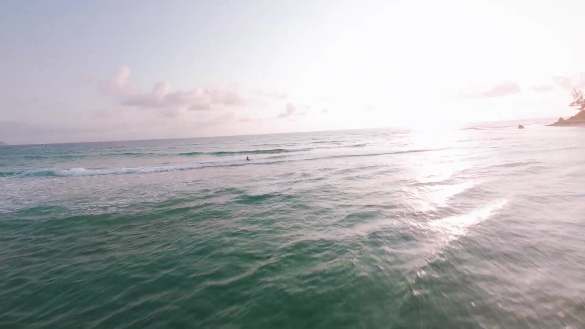 FPV drone flying low over the sea towards a beach at sunrise